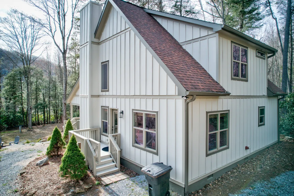 This exterior shot highlights the home's welcoming wooden steps, symmetrical window arrangement, and the lush greenery that surrounds the entrance. The porch area offers a tranquil spot to enjoy sunsets and socialize outdoors.