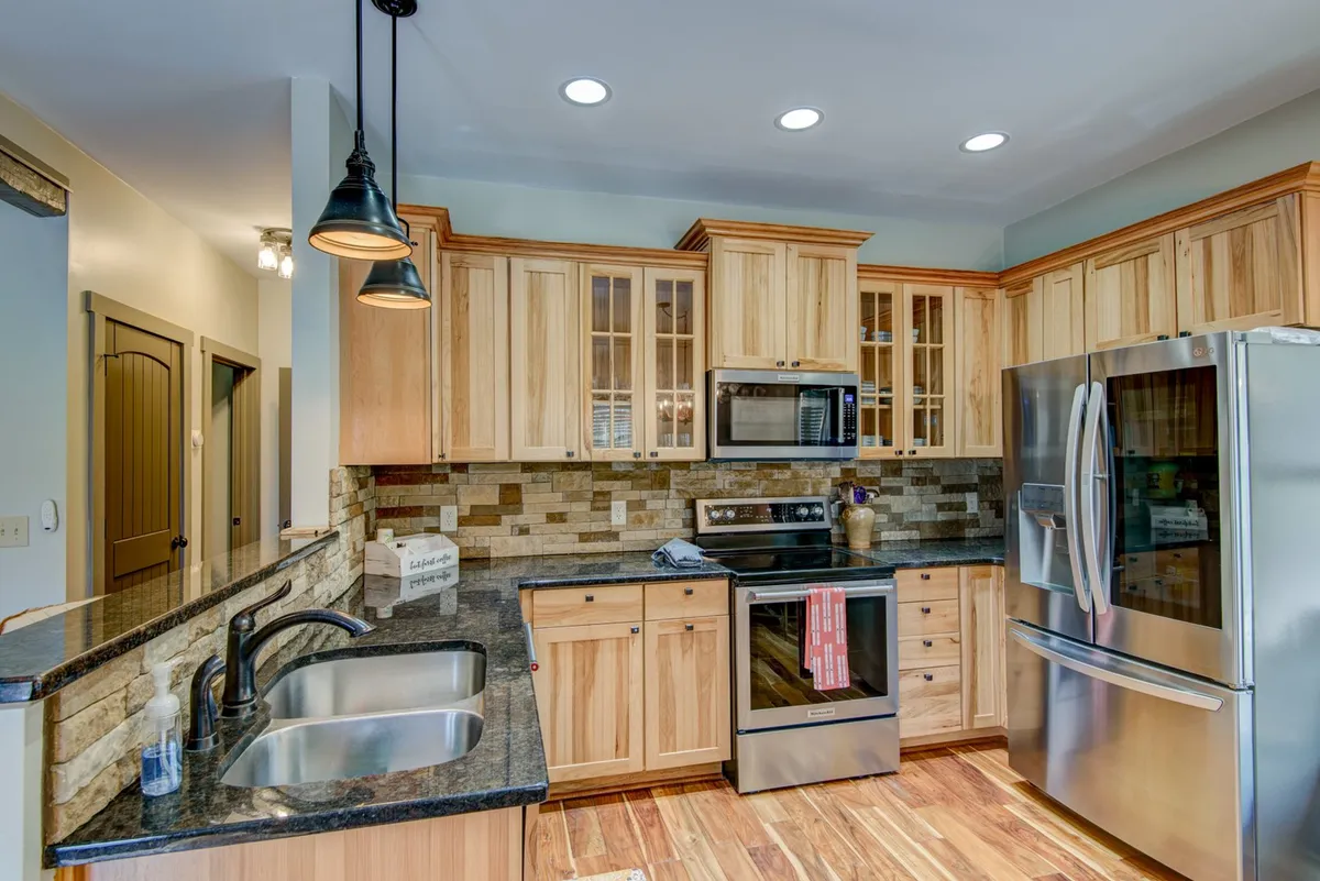 A modern kitchen featuring stainless steel appliances, granite countertops, wood cabinetry, a large island with a built-in sink, and a visible coffee station. The space is tidy and functional, ideal for cooking meals or preparing snacks.
