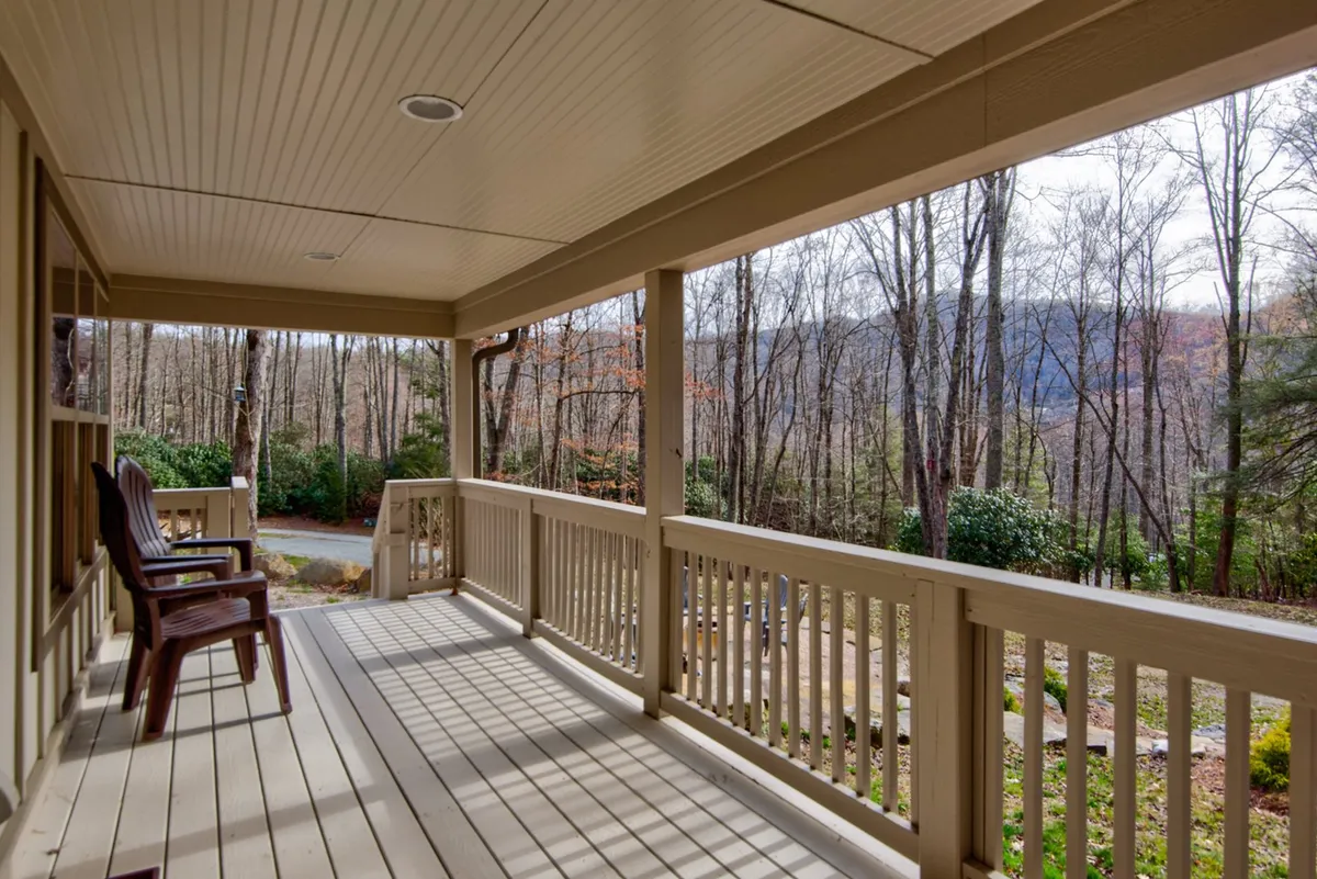 The image showcases a spacious wooden porch with classic rocking chairs facing out toward a view of trees and distant mountains. The porch setting is tranquil, with a natural backdrop ideal for relaxing, enjoying morning coffee, or stargazing on clear nights. The space emanates a sense of privacy and calm, making it perfect for a romantic retreat.