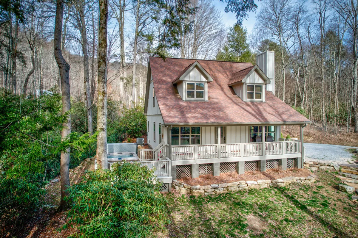 This image features the house nestled among tall trees, with a welcoming porch and ample outdoor space. The setting suggests the tranquility and natural beauty of the surroundings, ideal for guests and their pets to explore, relax, and enjoy nature walks. The presence of the porch hints at a space to unwind after a day of outdoor activity, while the surrounding landscape conveys the mountain adventure theme.