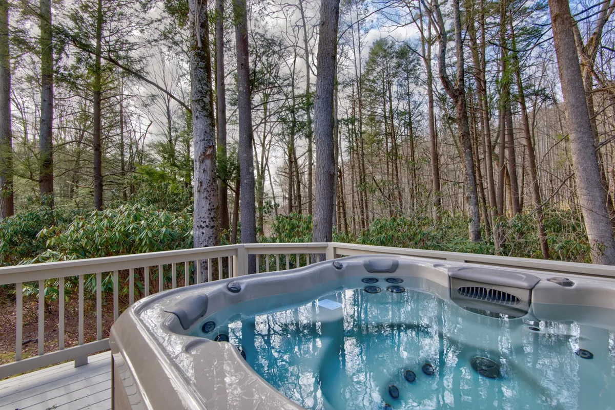 A peaceful deck scene featuring a hot tub nestled among the trees, offering an inviting spot for relaxation after a day of adventure. The wooden deck is surrounded by lush greenery, emphasizing the connection between comfort and the great outdoors.