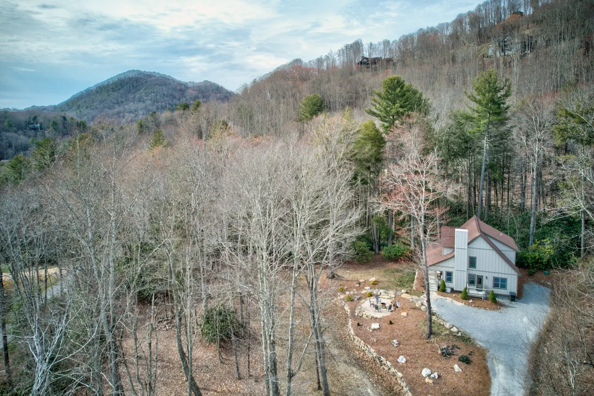This image features a view of the house nestled among lush trees, with a dedicated fire pit area in the foreground. The scene is serene, with a clear focus on outdoor gathering spaces—perfect for fireside relaxation, storytelling, and stargazing. It highlights both the home’s natural mountain setting and amenities tailored to romantic or intimate experiences.