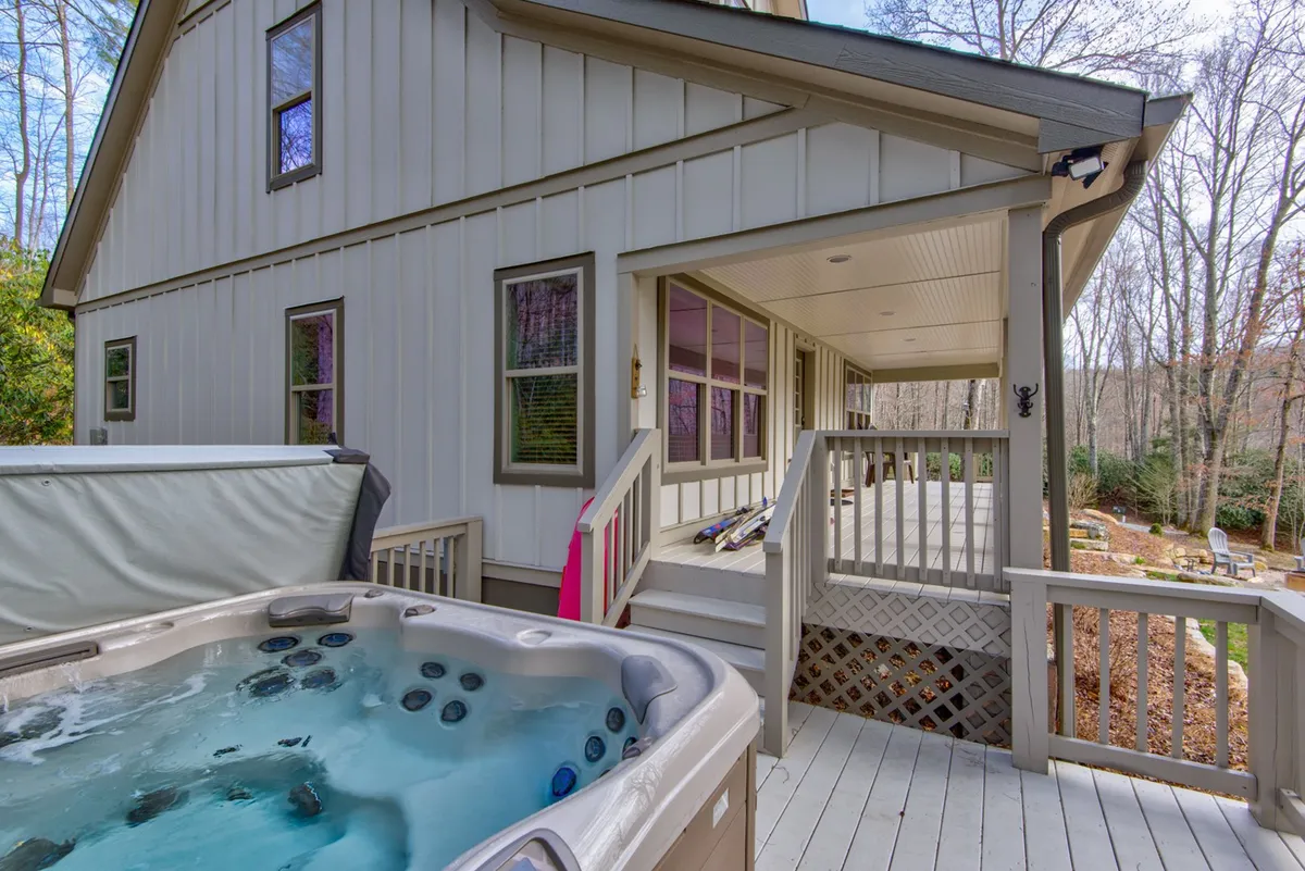 A tranquil wooden deck features a bubbling hot tub nestled among tall trees, with ample space for relaxing or entertaining. The inviting hot tub and the surrounding nature create an ideal spot for unwinding after a day of group activities.